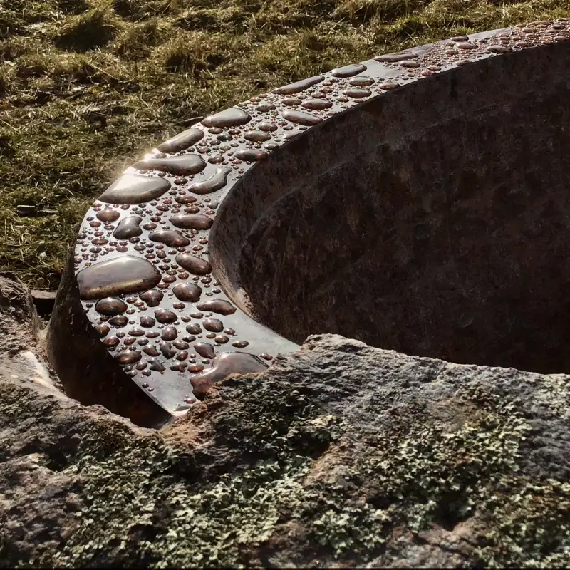 Puķu trauka fragments, kā saule iespīd rīta rasas lāsēs uz pulētas vāzes virsmas