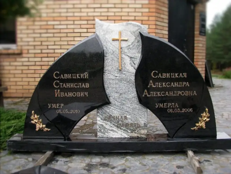 Kapakmens ar divām melnā granīta plāksnēm, kas aptver centrālo pelēko akmeni, uz kura ir piestiprināts zelta / bronzas krusts