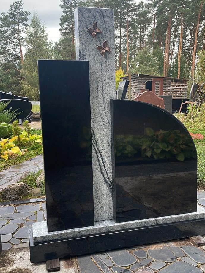 Augsts kapu piemineklis no trim plāksnēm – divām tumšām un vienas gaiši pelēkas